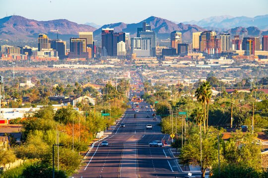 Downtown Phoenix skyline with mountains behind it, seen down a palm-lined avenue