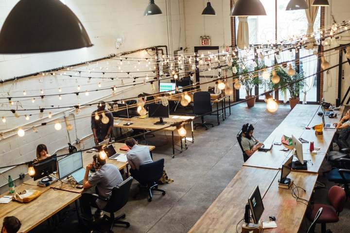 Coworking floor with people working at shared tables under string lights