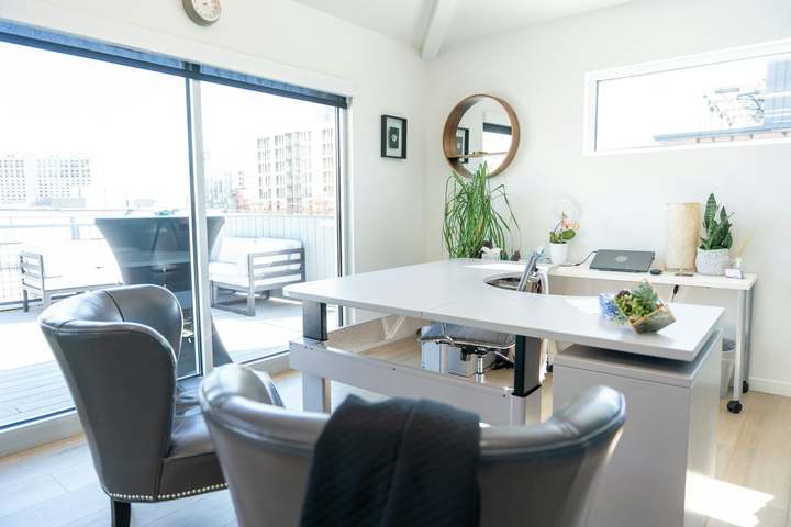 Sunlit private office with a white desk, lounge chairs, and plants